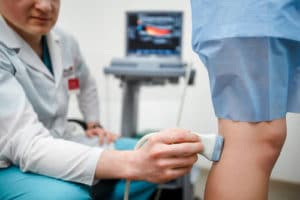 doctor doing ultrasound examination of patient's leg veins in his office