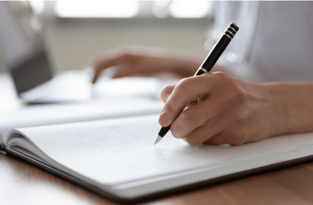 Woman nurse or pharmacist wearing white coat writing in paper notebook.