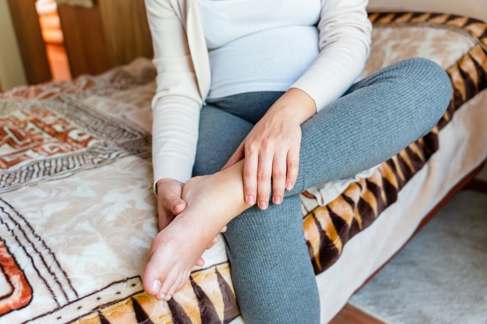 Pregnant woman on bed feeling her legs with varicose veins in Los Angeles